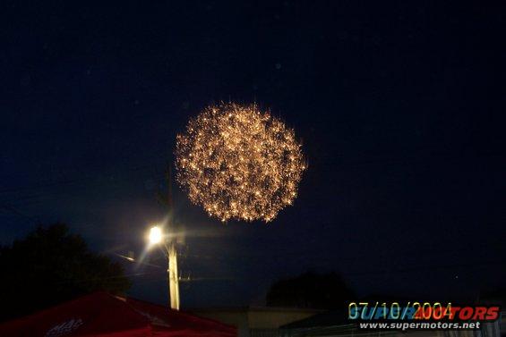 fireworks exploding in night sky over a street light and red canopy