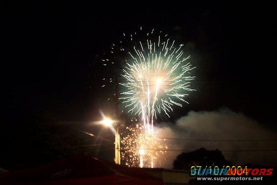 Fireworks explode in the night sky above a street light and dark trees