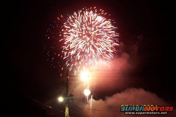 Fireworks explode in the night sky above a street light and power lines