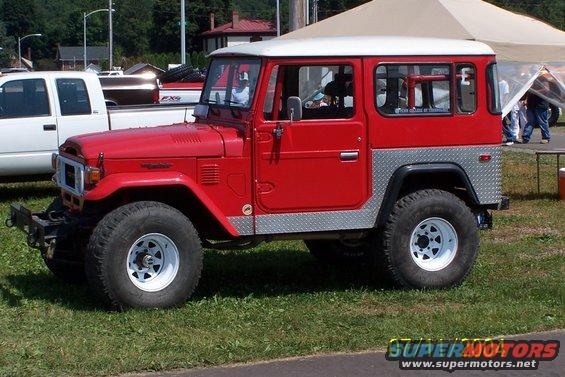 Red Toyota Land Cruiser FJ40 with white hardtop and diamond plate trim, parked next to a white pickup truck