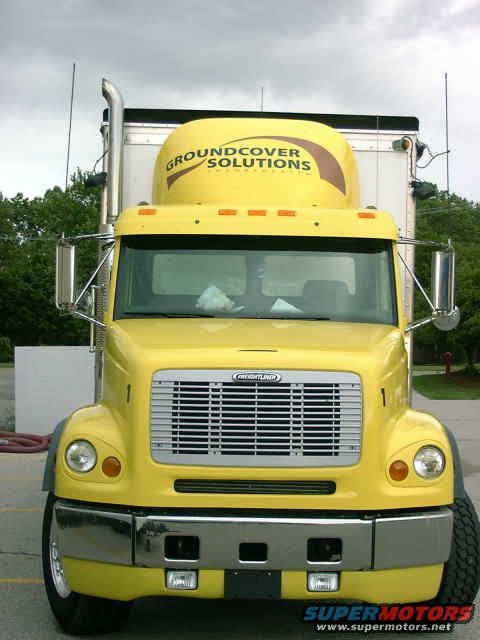 Yellow semi-truck front view. Groundcover Solutions logo on the sleeper. Chrome bumper and grille