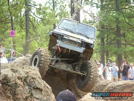 Off-road vehicle with large tires climbing rocks, front end lifted
