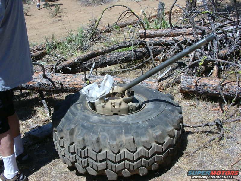 Tire with a jack extended from its center, lying on the ground amidst fallen branches