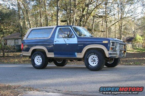 Blue and tan Ford Bronco parked on a road with trees in the background