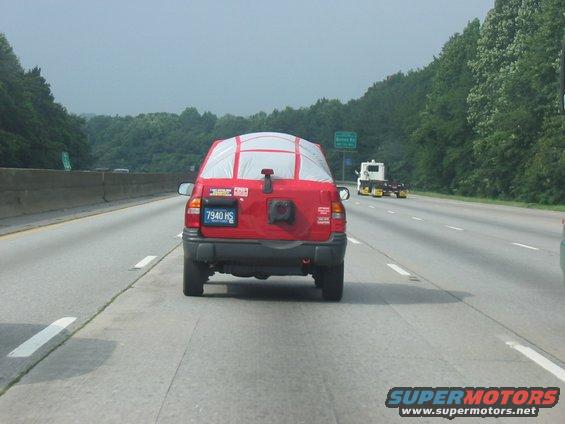 Red SUV with tarp on rear window, spare tire mount, and license plate 7940 HS