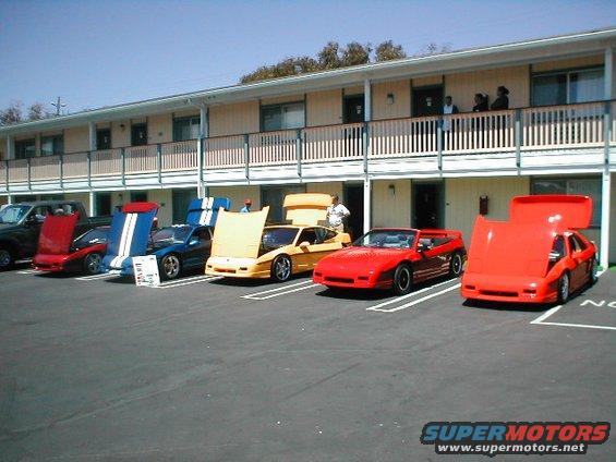 Several Pontiac Fieros parked in front of a motel, some with hoods up
