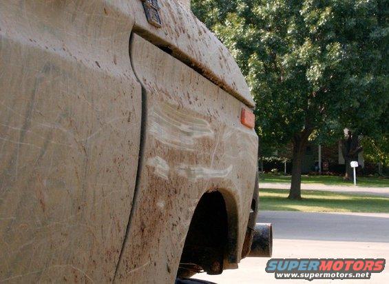Mud-splattered vehicle side with orange marker light and visible exhaust pipe