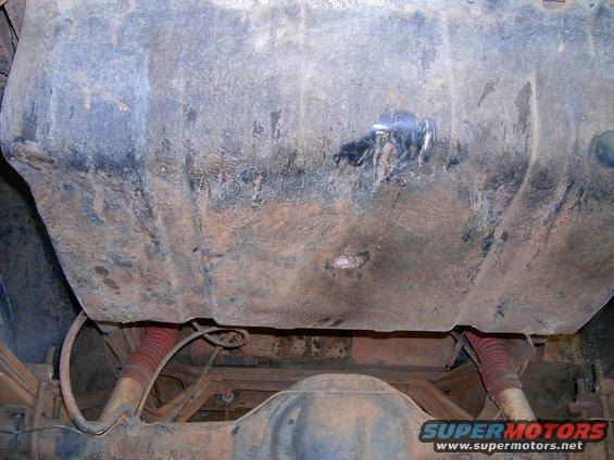 Underside view of a vehicle's fuel tank and rear axle with red shock absorbers