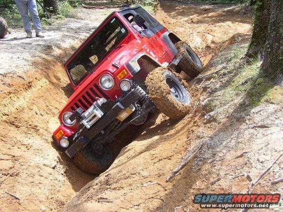 Red Jeep Wrangler tilted in a dirt ditch, tires covered in mud