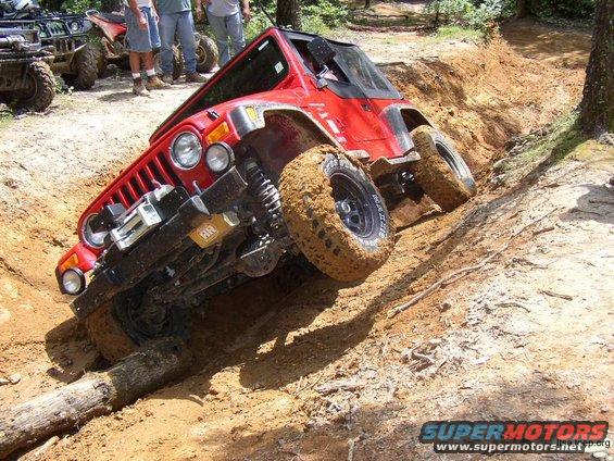Red Jeep Wrangler stuck on a muddy hill with a log, other ATVs and people in background