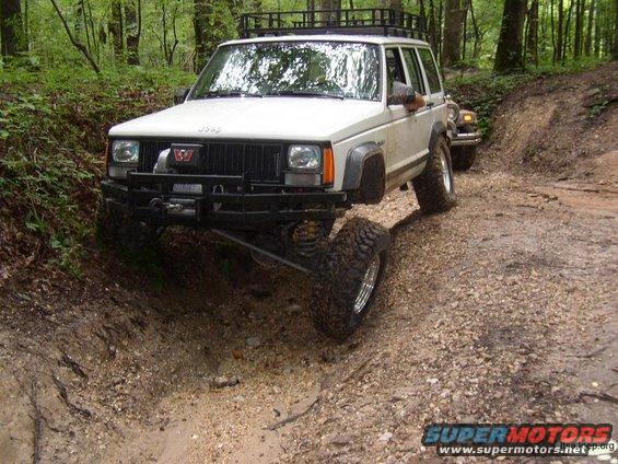 White Jeep Cherokee with off-road tires navigating a dirt trail