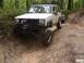 1984 Ford Bronco - A white Jeep Cherokee, modified for off-roading, tackles a challenging dirt path with another vehicle visible behind it.