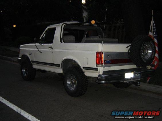 White Ford Bronco parked at night, rear view. Spare tire mounted on the back