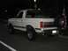 1988 Ford Bronco - This white Ford Bronco is parked on a street at night, showing its rear profile and spare tire.