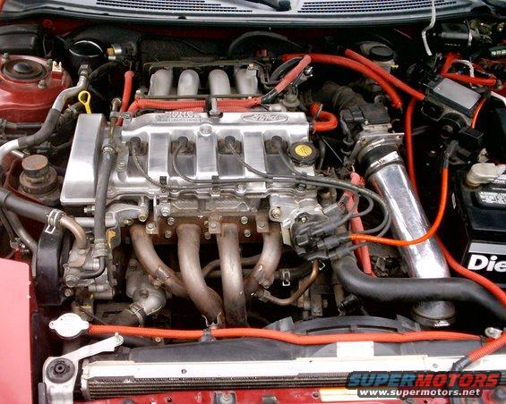 Close-up of a car's engine bay with red hoses and silver intake pipe