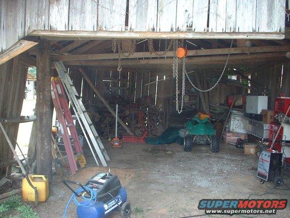 Cluttered barn interior with ladders, tools, an air compressor, and a green ATV