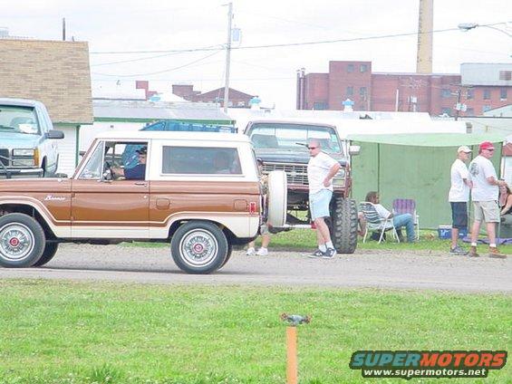 Brown and white Ford Bronco parked next to a lifted pickup truck with people standing around