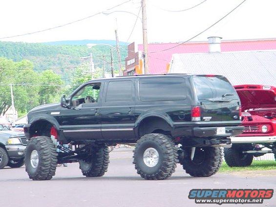 Lifted black SUV with oversized tires parked next to a red pickup truck