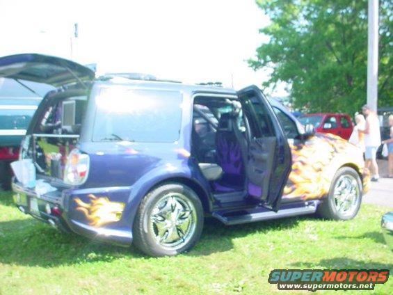 Purple SUV with flame decals and chrome rims, doors open. Another vehicle is parked nearby