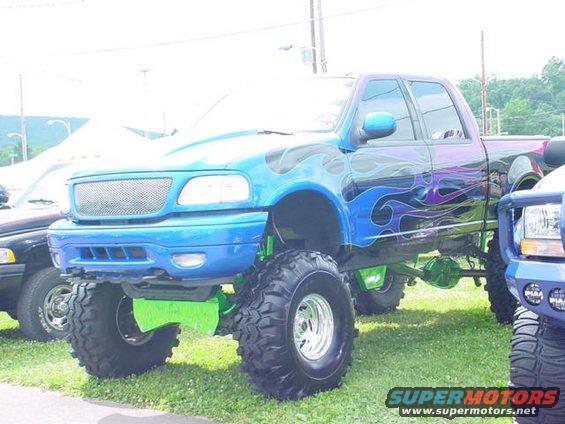 Blue pickup truck with flame graphics, lifted suspension, and large tires
