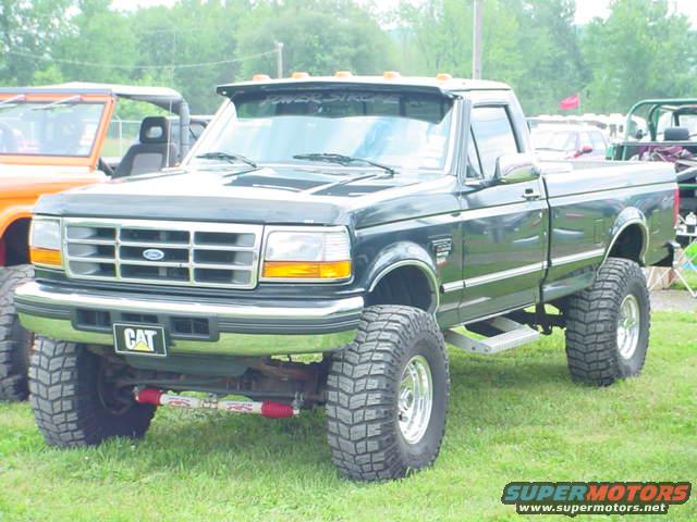 Black Ford F-Series pickup truck lifted with large tires. Orange Jeep visible to the left