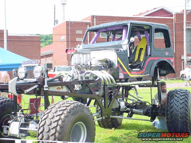 Custom monster truck with large tires, exposed engine, and roll cage. A man is working on it
