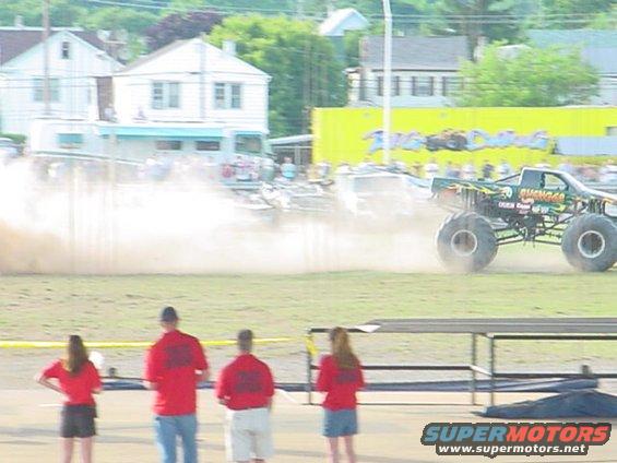 Monster truck driving through dust with spectators watching