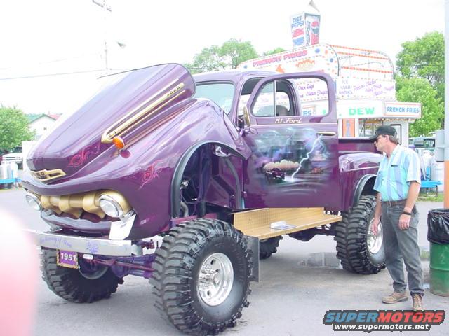 Purple 1951 Ford pickup with custom paint and large tires. Hood and door are open. Man stands next to it