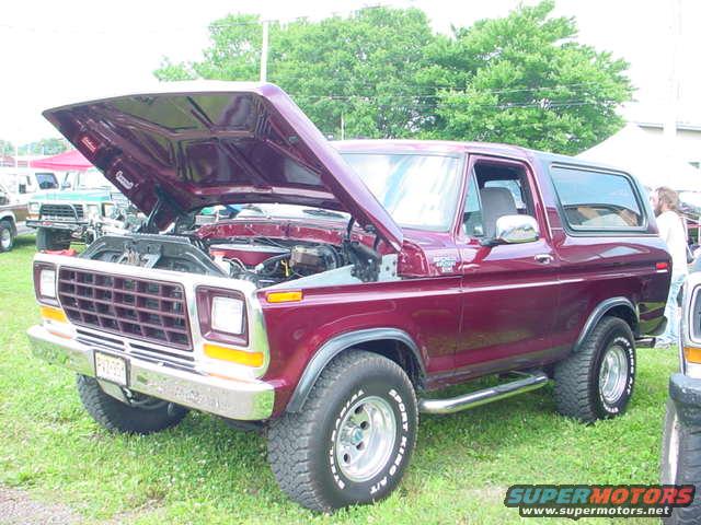 Maroon Ford Bronco with hood open, parked on grass. Another vehicle is partially visible to the right