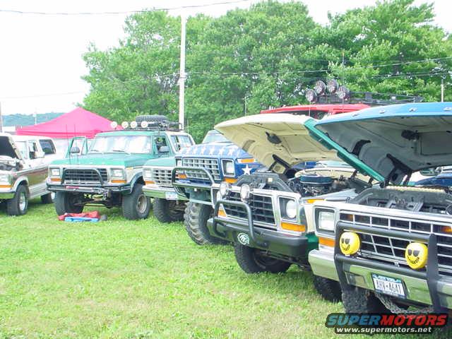 Several 1979 Ford Broncos and trucks parked on grass, hoods open