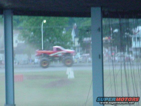Red monster truck with white and yellow graphics mid-air jump