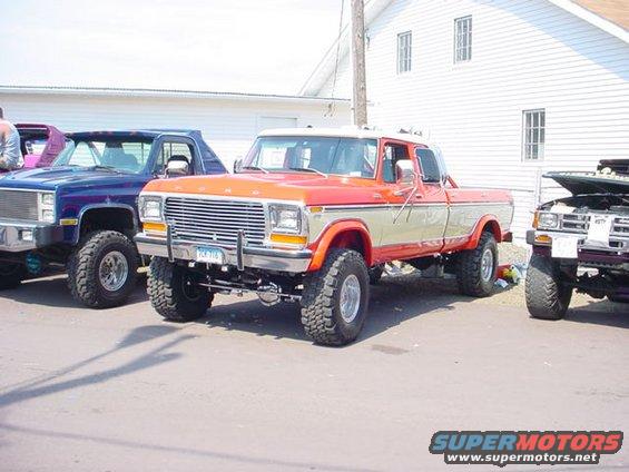 Orange and tan pickup truck with lifted suspension and chrome grille. License plate reads '704 116'