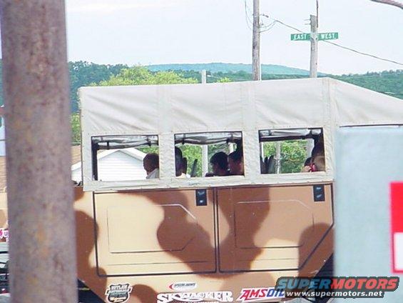 Camouflaged truck with canvas top, windows showing passengers, and logos on the side
