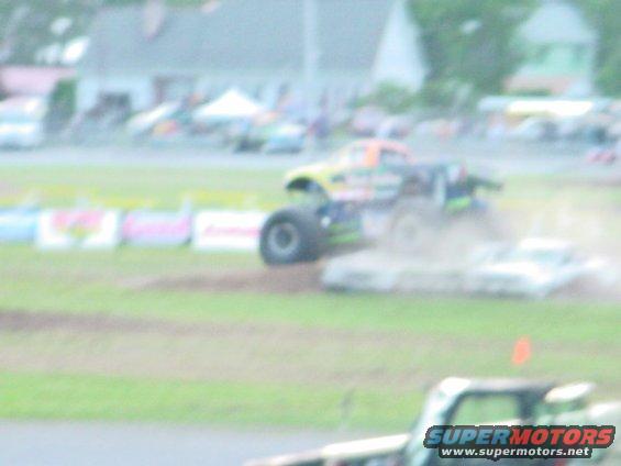 Monster truck driving over crushed cars on a dirt track