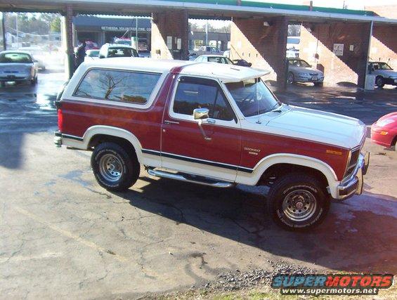 1986 Ford Bronco parked outside a car wash, red and white two-tone paint, white removable top