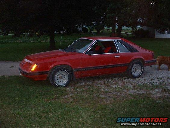 Red coupe car with a black side molding and silver wheels, parked on a gravel driveway
