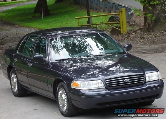 Dark sedan parked on a paved surface with trees and a yellow fence in the background