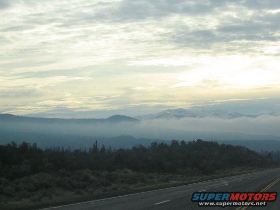 Roadway stretching into a misty landscape with mountains in the distance under a cloudy sky