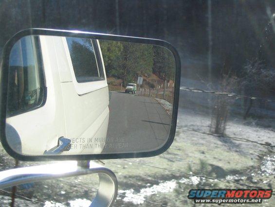 White van side mirror reflection shows green SUV on a rural road