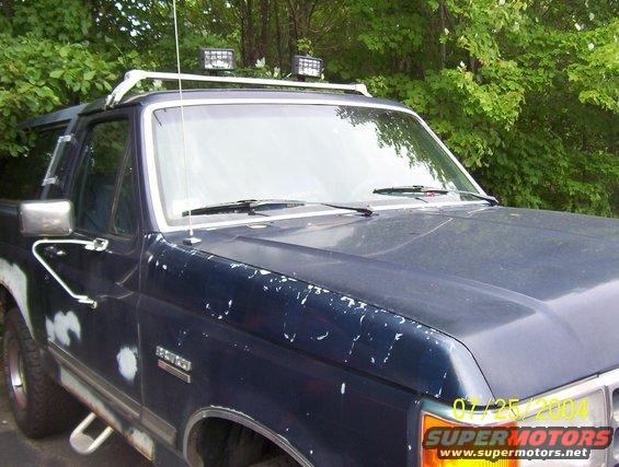 Dark blue 1989 Ford Bronco with roof rack and auxiliary lights, showing paint damage and primer spots