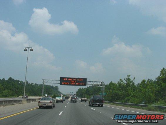 Highway traffic under a sign displaying 'AIR QUALITY ALERT TODAY REDUCE YOUR DRIVING'