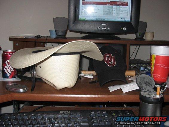 Desk with a cowboy hat, baseball cap, Dr. Pepper can, and a computer monitor