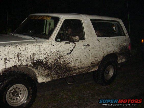 Mud-splattered white 1987 Ford Bronco, driver's side view, at night