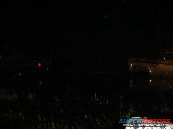 Two trucks are being towed at night, one with its taillight illuminated