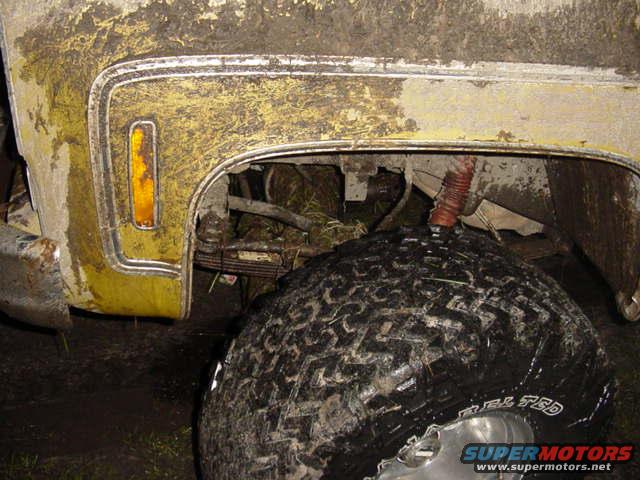 Mud-covered yellow vehicle fender with amber marker light and large off-road tire