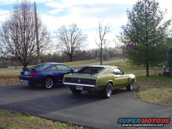 Green 1970 Ford Mustang parked on asphalt, rear view with louvers on back window