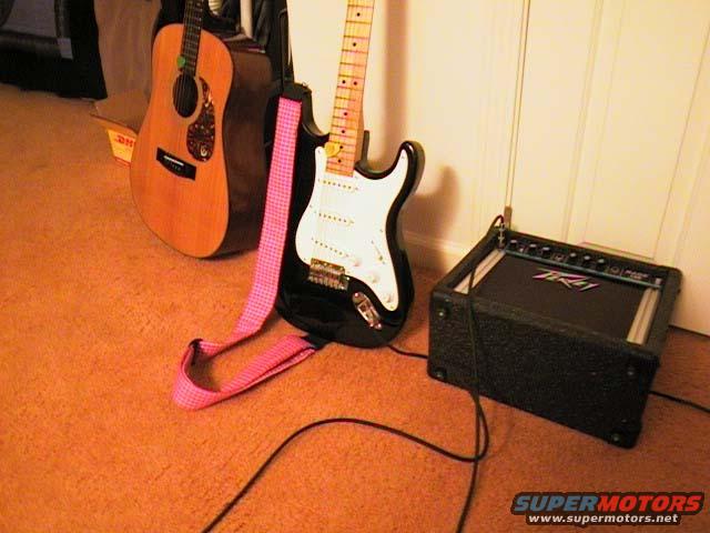 Black electric guitar with pink strap and acoustic guitar next to a Peavey amplifier