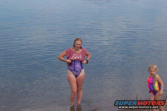 Woman in swimsuit and child in life vest by water