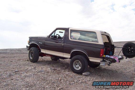Brown and tan 1992 Ford Bronco with a spare tire mounted on the rear, parked on a rocky surface