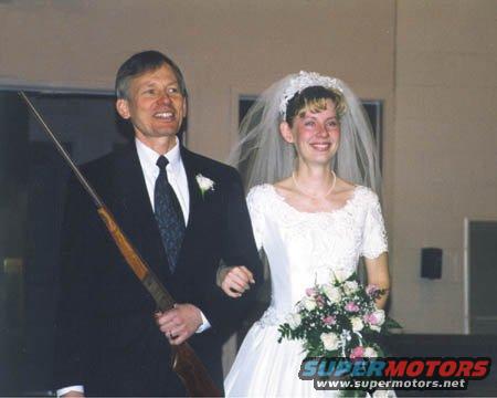 Man in suit holding a rifle walks with a bride in a wedding dress